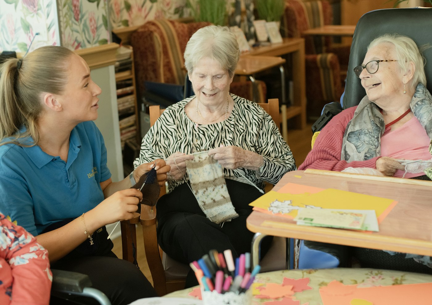 Caregiver assists two elderly women knitting